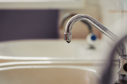 Water drop drips from rusty steel tap in bathroom or kitchen. Plumbing concept.