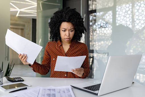 Upset and unsatisfied woman at workplace, businesswoman boss checking documents, accounts and contracts, financial woman got bad results in financial reports, working inside office with laptop.