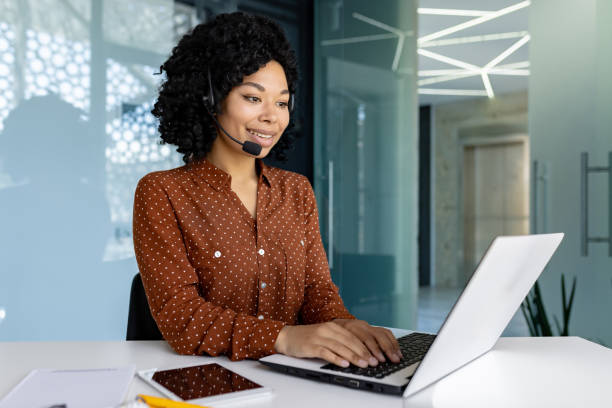 istock Young beautiful office worker using headset microphone and laptop for video call, businesswoman typing on keyboard smiling satisfied with achievement results successful African American woman 1692577123