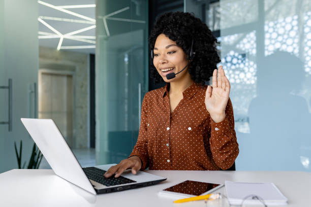 istock Woman with headset phone using laptop for remote communication and video call, african american woman waving at camera greeting 1692577130