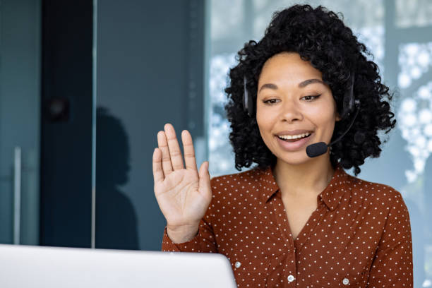 istock Woman with headset phone using laptop for remote communication and video call, african american woman waving at camera greeting 1692577655