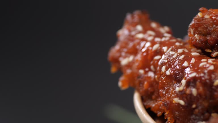 Spicy chicken wings doused in sauce swirl in a paper bucket. Close up.