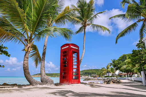 Traditional English red telephone booth on a the beach of Dickenson Bay on Antigua Island.