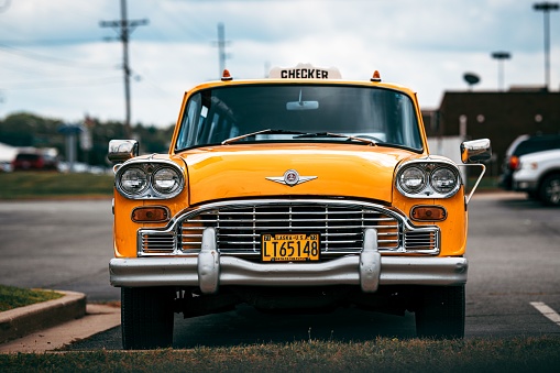 Angola, United States – October 01, 2022: A bright yellow taxicab parked in a city street with a retro look