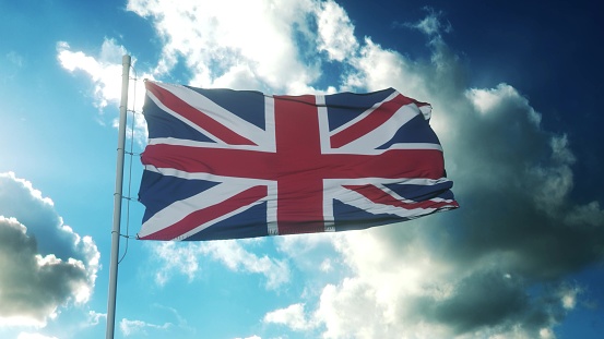 Flag of United Kingdom waving in the wind, sky and sun background. United Kingdom Flag. 3d illustration.