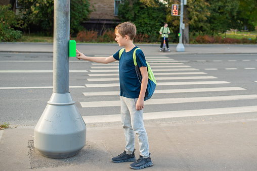 the boy presses the traffic light button, stands in front of the pedestrian crossing, is about to cross the road
