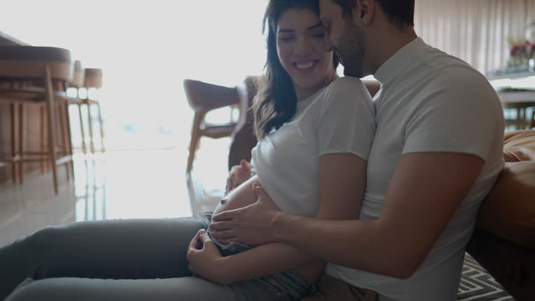 Pregnant couple embracing while talking and touching the belly in the living room at home