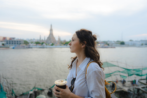 Young woman  drinking coffee and looking at Wat Arun and Chao Phraya river