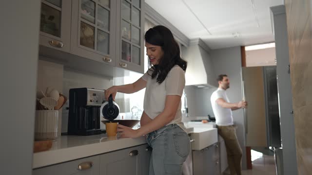 Pregnant woman pouring coffee into cup and talking with her husband in the kitchen at home