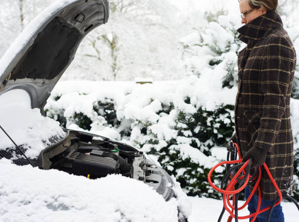 Woman working on broken down car in snow  jumper cable stock pictures, royalty-free photos & images