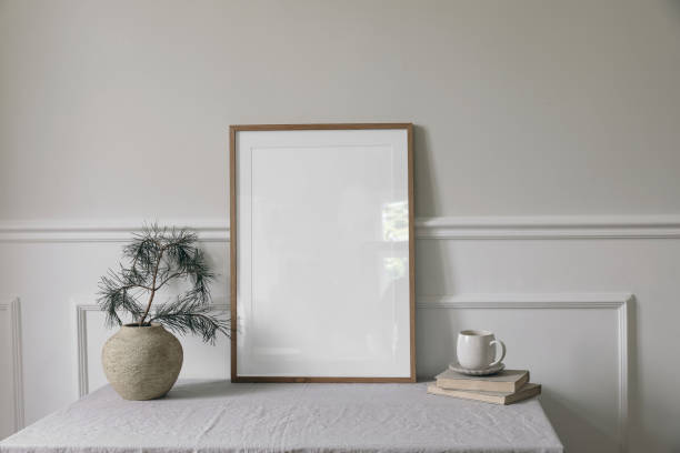 istock Moody Christmas Scandinavian interior. Minimal winter artistic composition. Blank vertical wooden picture frame mockup, cup of coffee on table. Pine tree branches, old clay vase. White wall background 1692728738