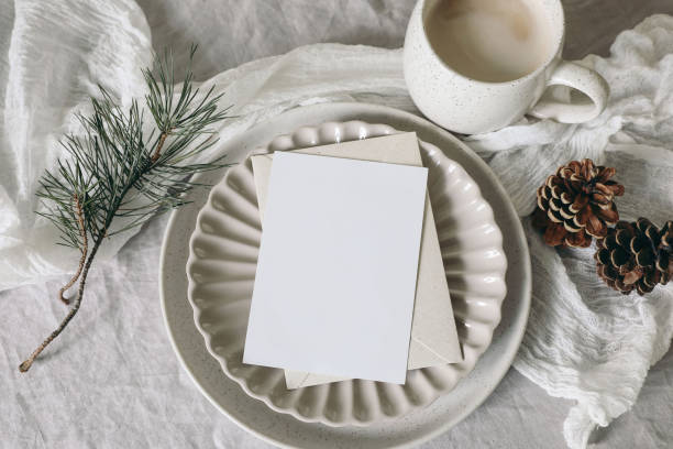 istock Christmas still life. Blank greeting card, invitation mockup on ceramic plate. Pine cones and pine tree branches on white linen tablecloth. Cup of coffee, winter breakfast. Festive holiday flat lay 1692731468