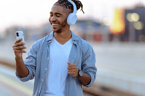 Smiling African American young man using a smart phone while waiting for transportation