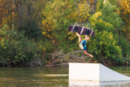 An athlete jumps from a springboard. Wakeboard park at sunset. A man performs a trick on a board.