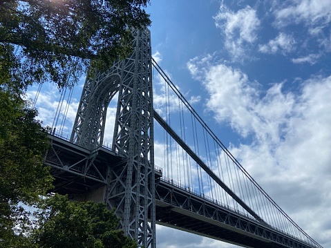 Looking up view of one of the towers of the George Washington Bridge through the branches of a tree from a pedestrian and bike path in a park in Washington Heights, New York City