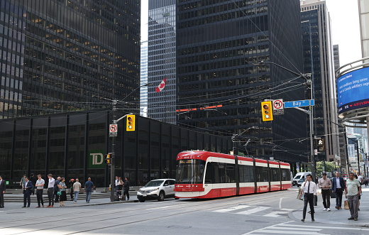 Toronto, Canada - August 21, 2023: Looking from the northeast corner of Bay Street at King Street West. The TTC King streetcar heads east on King Street West. Pedestrians and traffic in the Financial District share the intersection lined with sleek bank towers. Summer afternoon with hazy skies from distant wildfires.