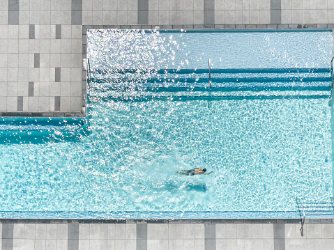 Looking down on a man swimming in a large, chic pool from a high point of view