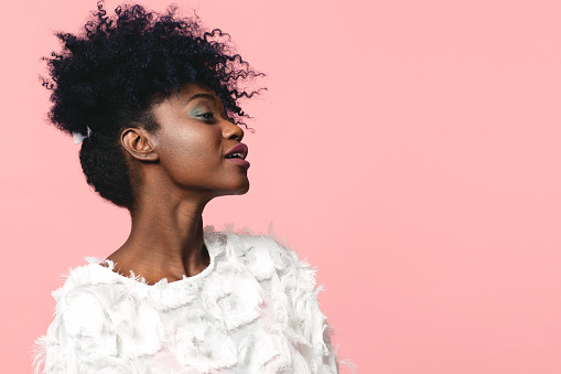Portrait of a lovely young girl with afro curly hair looking up, isolated on a pink background