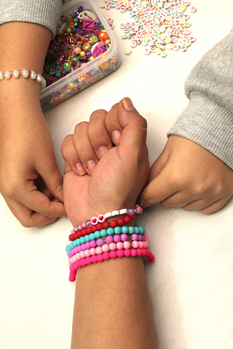 Hands of teenage women make and exchange friendship bracelets as a fashionable craft