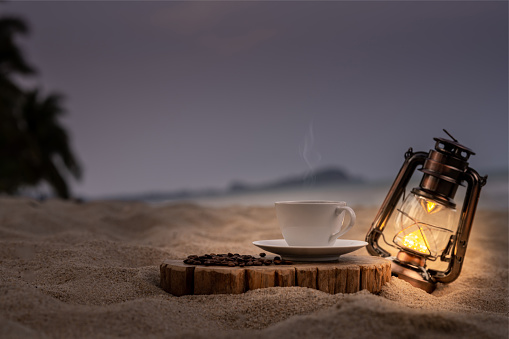 Close-up white coffee cup and many coffee beans placed around on wood table with a beautiful seascape of nature background, concept coffee vacation travel.