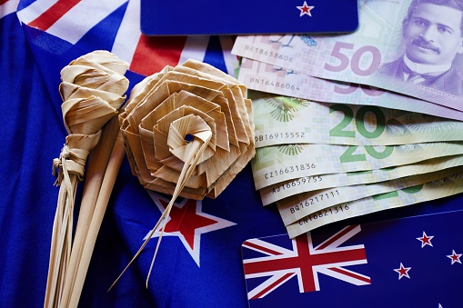 A mixture of New Zealand Bank notes and coins with New Zealand flags and Putiputi flowers, a symbol of bicultural New Zealand kiwiana.