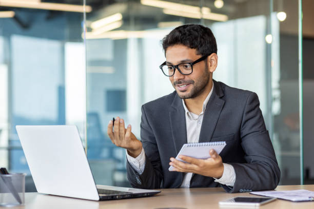 istock Young successful hispanic man watching online video kur webinar, businessman studying at workplace inside office, writing data in notebook, man improving skills qualification 1693003760
