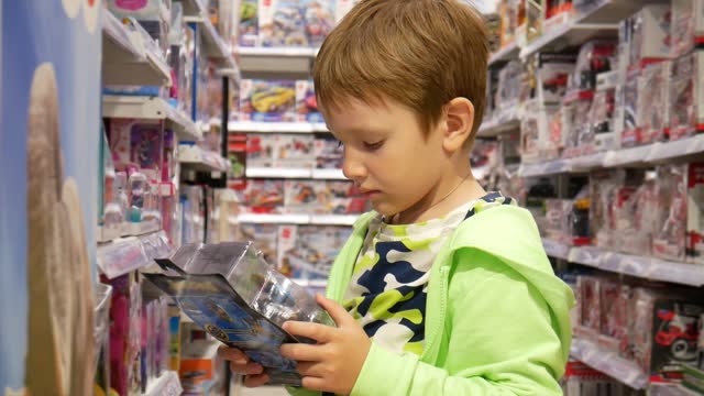 A cute boy takes a box with a toy in a toy store and examines it
