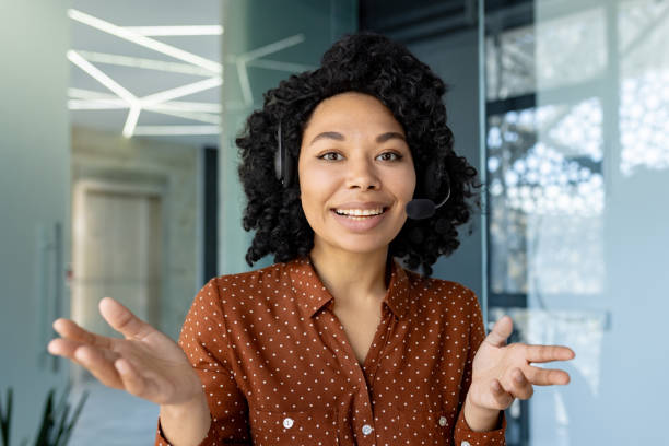 istock Webcam pov view, video call young beautiful woman with headset phone talking remotely with clients and partners, employee smiling and looking at camera, working inside office 1693004043