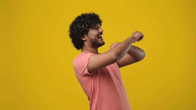 Young indian bearded guy with curly hair wearing t-shirt dancing over orange studio background