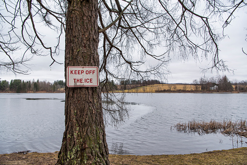 A keep off ice sign on a single tree on the edge of the water at Taconic State Park, Rudd Pond, in millerton New york.
