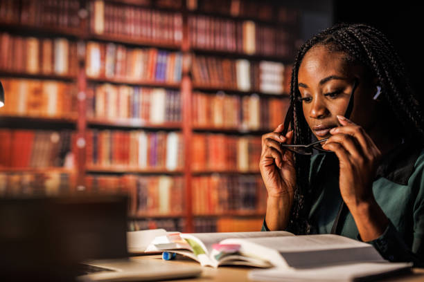istock Young woman putting on her reading eyeglasses when studying at the library 1693026895