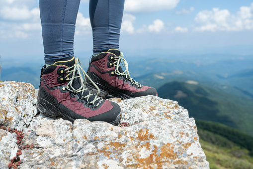 Low point of view of unrecognizable female hiker stepped on a rock in the mountains.