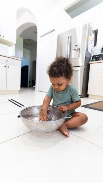 Cute little mixed race toddler boy in the family kitchen playing with cooking tools, colander stock photo