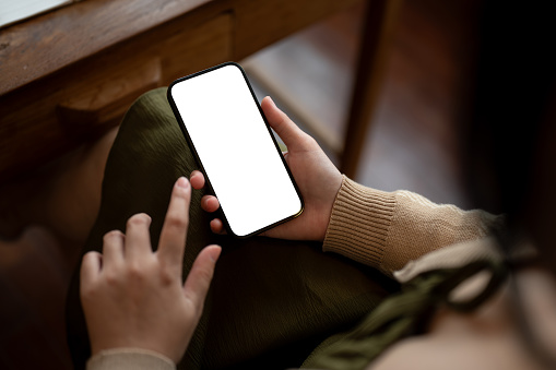 Close-up image of a woman using her smartphone while relaxing in a coffee shop. White screen smartphone mockup in a woman's hand. mobile application, texting, responding to messages, social media