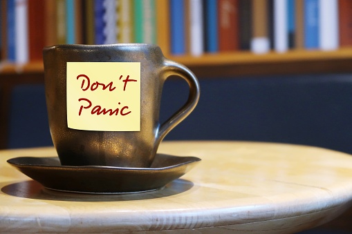 Coffee cup and note on orange background with text written DON'T PANIC , to calm down anxiety and stay chilled when life gets stressful or fear of coronavirus pandemic