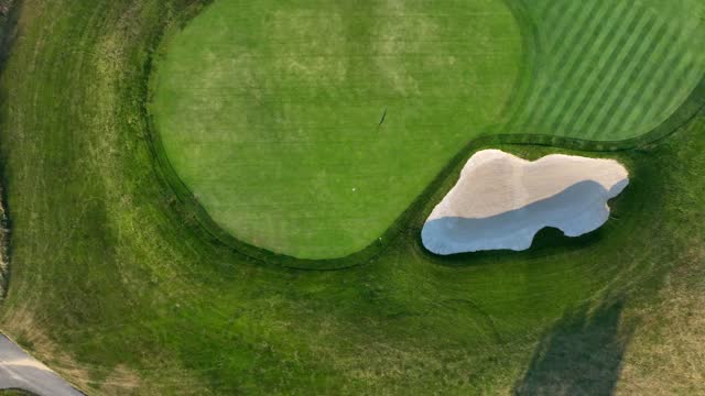 Golf course hole with flag. Aerial rising shot of prestigious green revealing sand bunker and rough. Sunset at country club.