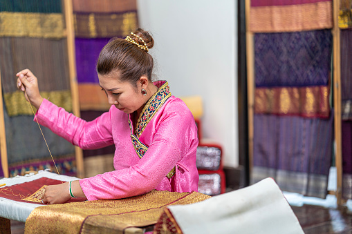 Crafts and craftsmanship.  Asian woman embroidering golden thread on silk. Yong woman are Sewing silk.