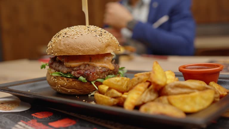 SLO MO Closeup of Hamburger Loaded with Cheese and Fries Served on Tray in Restaurant