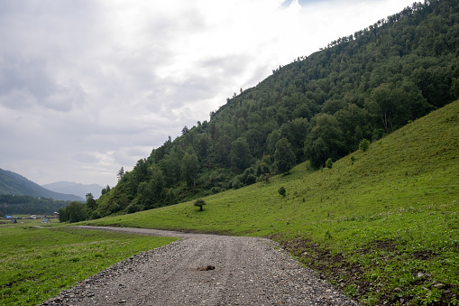 A country road between fields with hay bales in autumn in the mountains. Agricultural field with sky and clouds. The nature of agriculture. Straw in the meadow. Rural natural landscape.