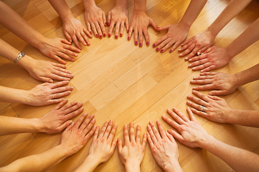 Group of women (team) in circle hands on the floor. Having fun while relaxing and stretching in a gym after pilates. Circle of hands.