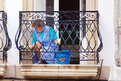 Woman cleaning cast iron balcony seen from the street, traditional stone house,Betanzos, A Coruña province, Galicia, Spain.