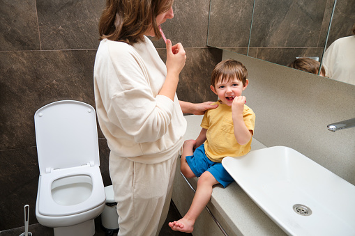 Mom and baby are brushing their teeth. Kid aged two years (two-year-old boy)Mother and child having fun in the bathroom.