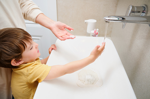 Mother washing hands with soap and water in the bathroom with her baby. Kid aged two years (two-year-old boy)