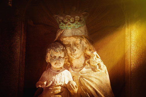 Queen of Heaven. Ancient statue of the Virgin Mary with Jesus Christ in sunlight.