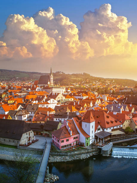 This captivating aerial view captures the picturesque charm of Cesky Krumlov during the serene moments of sunset. This UNESCO World Heritage Site in the Czech Republic is bathed in the warm, golden hues of the setting sun. The image showcases the medieval architecture and old town of Cesky Krumlov, with historic buildings and churches creating a mesmerizing cityscape along the banks of the Vltava River. The rooftops of centuries-old houses are silhouetted against the colorful twilight sky. Cesky Krumlov's urban skyline, steeped in Czech culture and history, becomes even more enchanting as the day gracefully transitions into evening. It's a scene that beckons travelers to explore its historic streets and experience the magic of this timeless city.