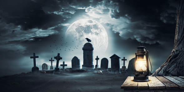 Scary cemetery with ancient graves and old lit lantern in the foreground