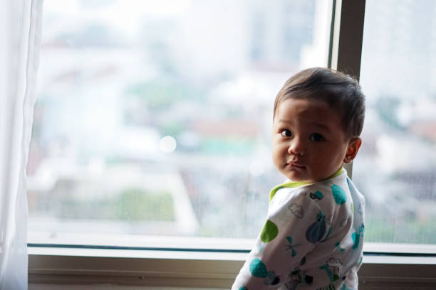 istock Asian baby boy looking out the apartment window while waking up 1693346475