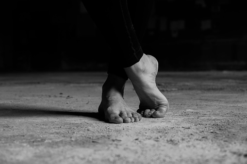 The bare feet of a woman dancer standing on concrete floor.