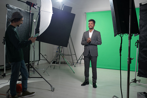 Filming process of TV program with presenter standing against the green background and telling the news