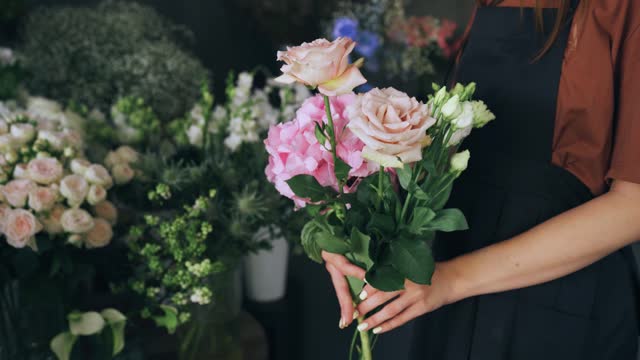 Close-up, hands of a woman seller, a florist in an apron holds flowers in a flower shop.